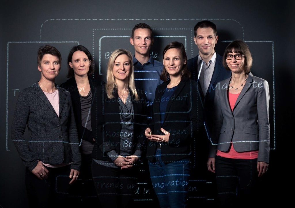 Portrait of research team of Swiss Observatory for Vocational Education and Training, standing in front of a diagram of their research activities